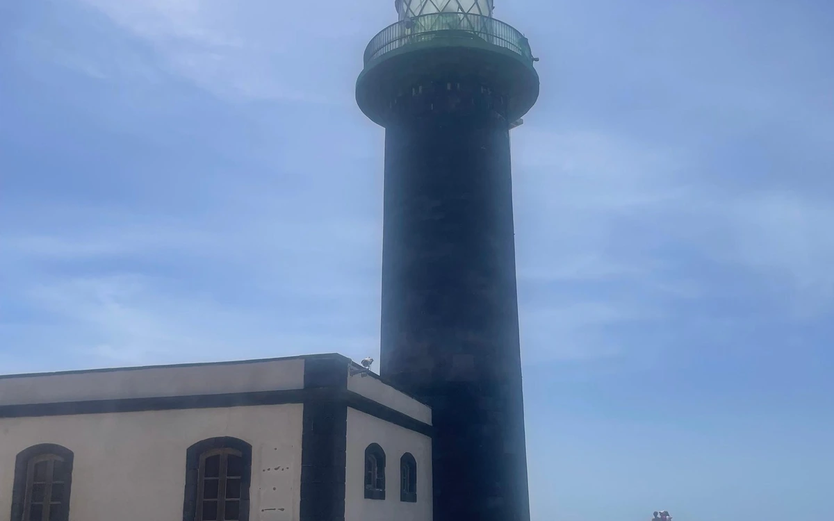 Ein schwarzer Leuchtturm neben einem niedrigen weißen Gebäude unter blauem Himmel