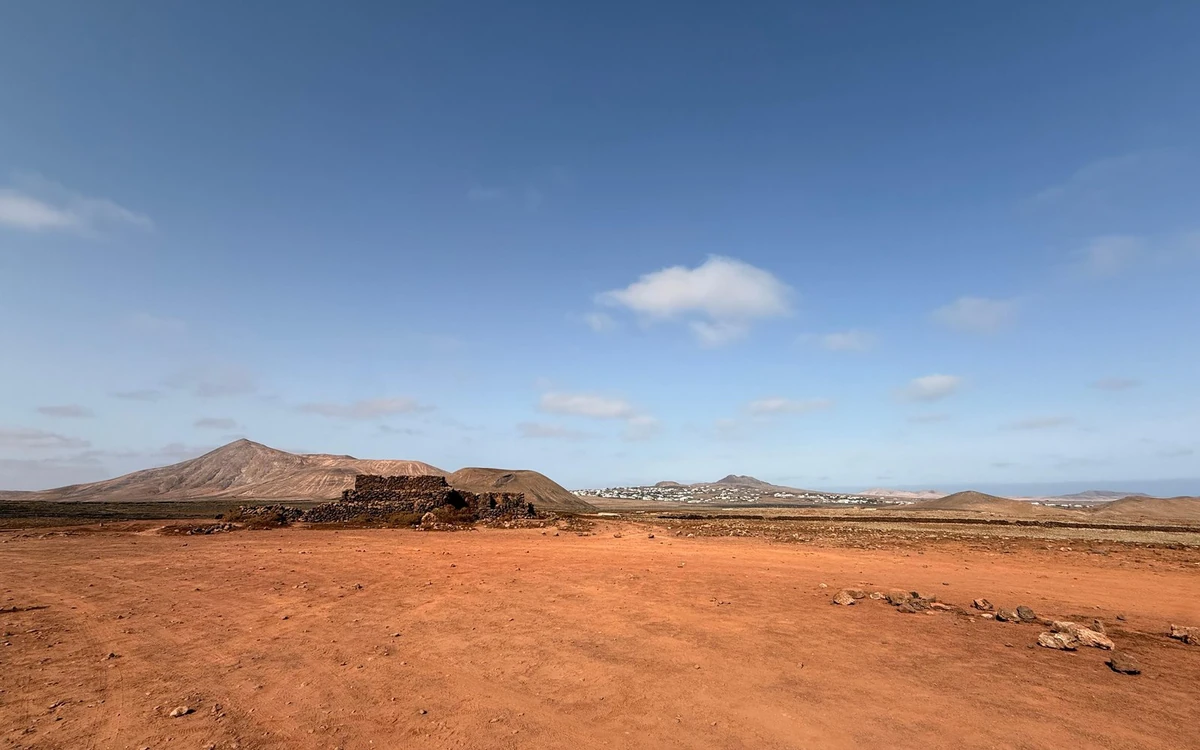 Flache rote Erde mit niedrigen braunen Hügeln unter blauem Himmel mit Wolken