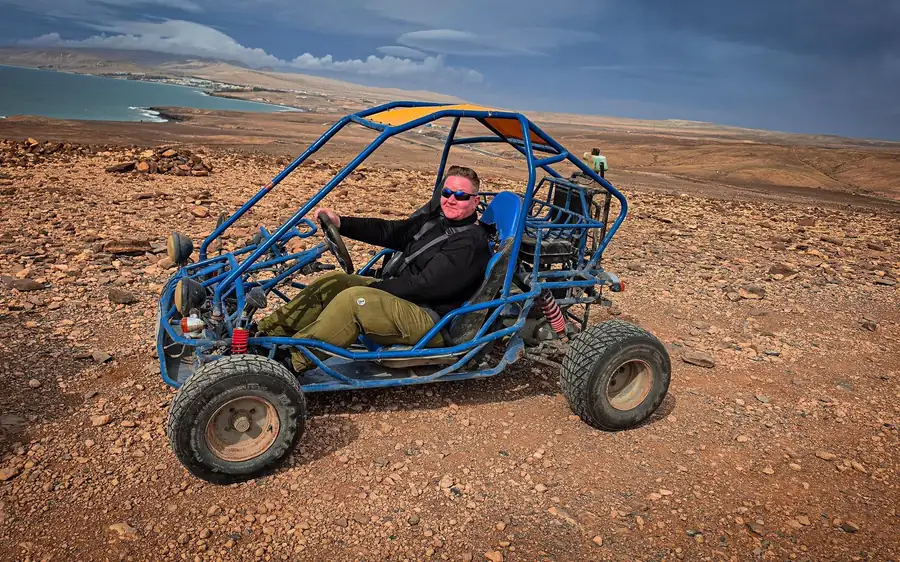 Ein Fahrer in einem offenen Buggy mit blauem Rahmen auf roter Erde über der Küste