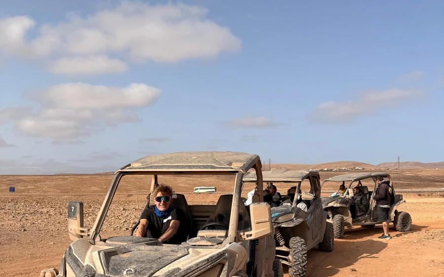 Ein Junge am Steuer eines staubigen Buggys, dahinter weitere Buggys im Sand