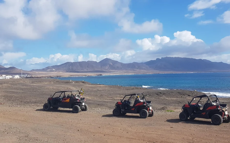 Drei Buggys auf einem Küstenplateau mit Bergen und Meer im Hintergrund