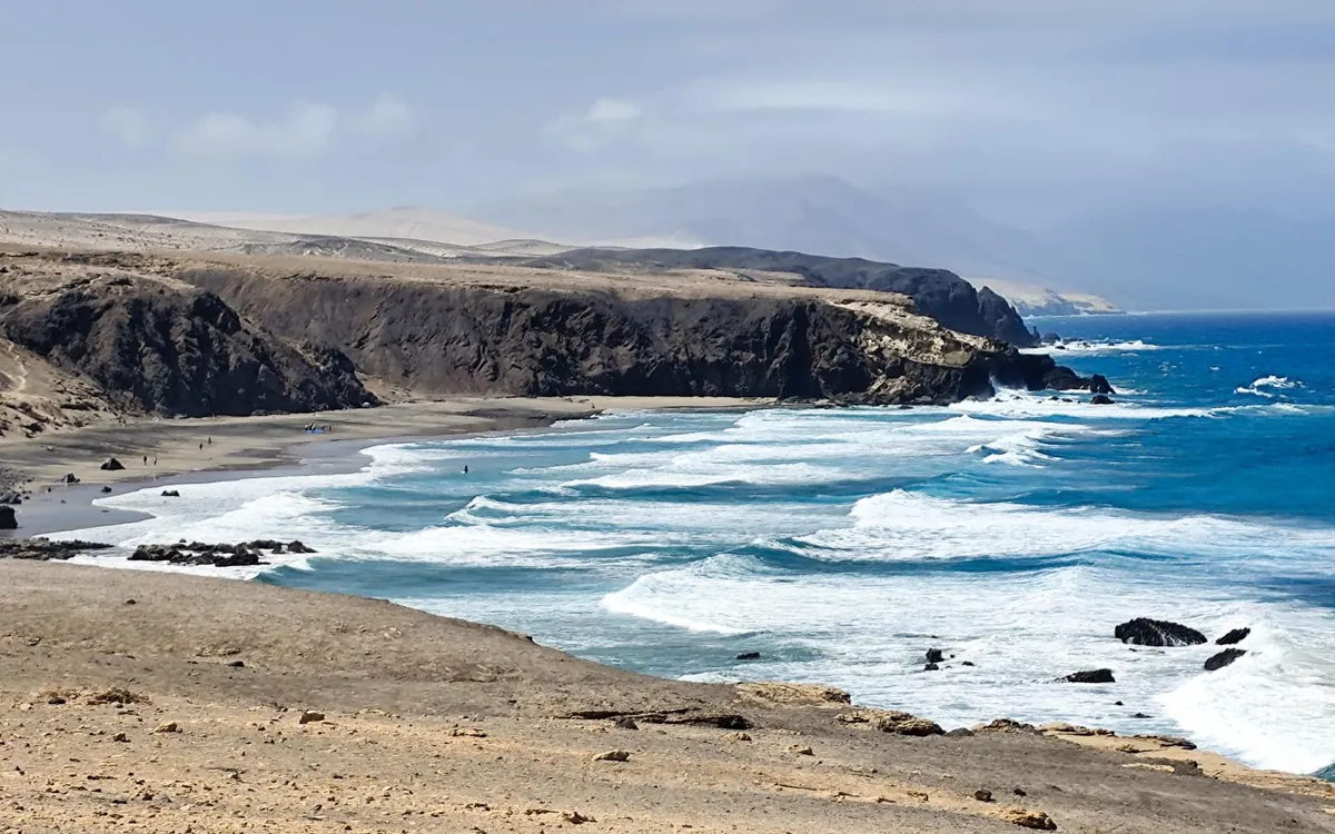 Wellen brechen unter dunklen Klippen an der Westküste von Fuerteventura